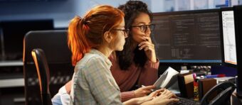 two women sitting in front of a computer screen